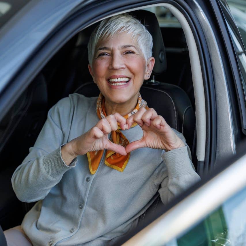 Happy woman gesturing heart shape sitting in car at showroom